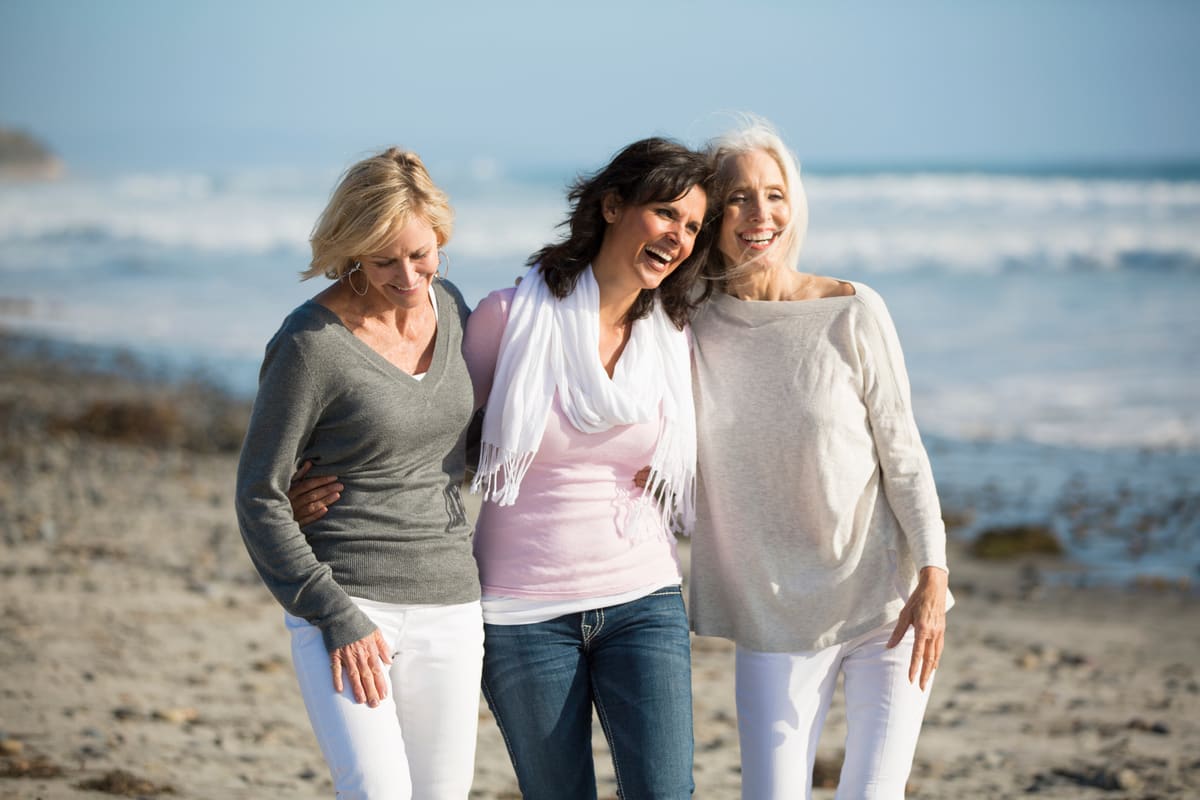 Three women walking together along a beach, laughing