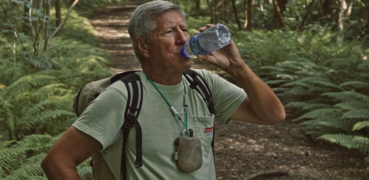 A man pausing on a bush walking track for a drink of water