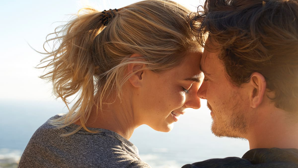 A couple standing forehead to forehead in the sun, both smiling