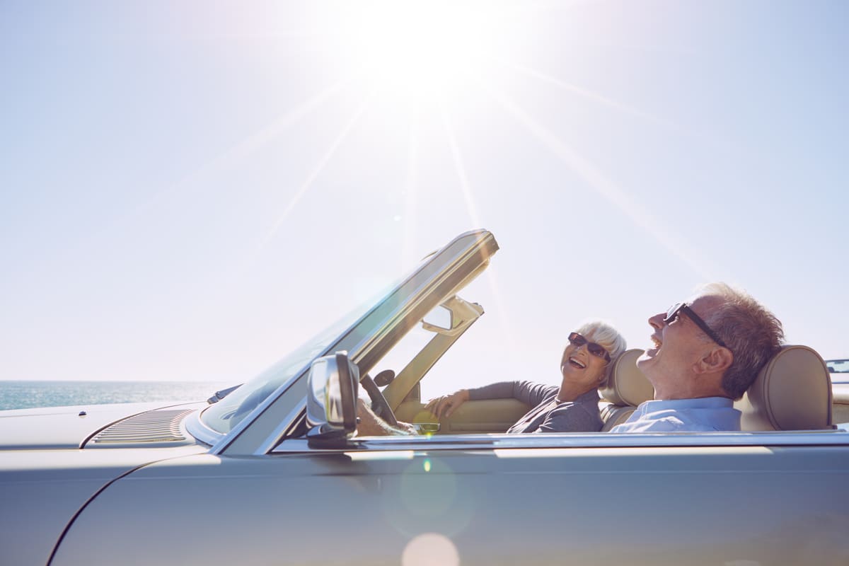 A couple in their sixties laughing in an open-top car on a bright day