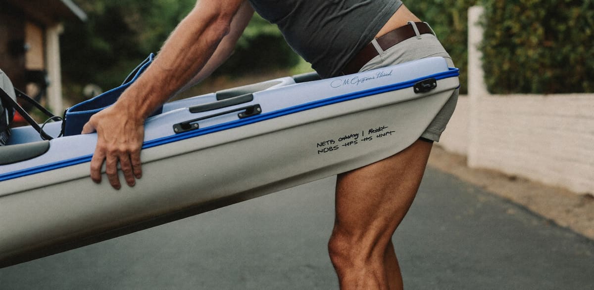 A man lifting a sea kayak in his driveway, knees bent and back straight