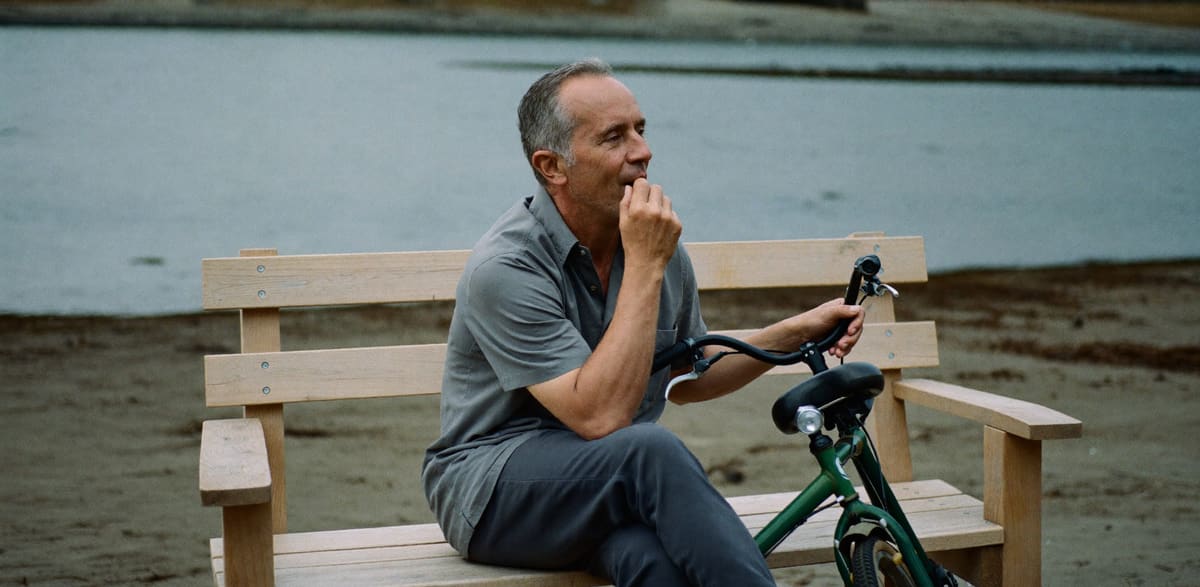 A man taking a breather on a bench beside an estuary, bicycle alongside