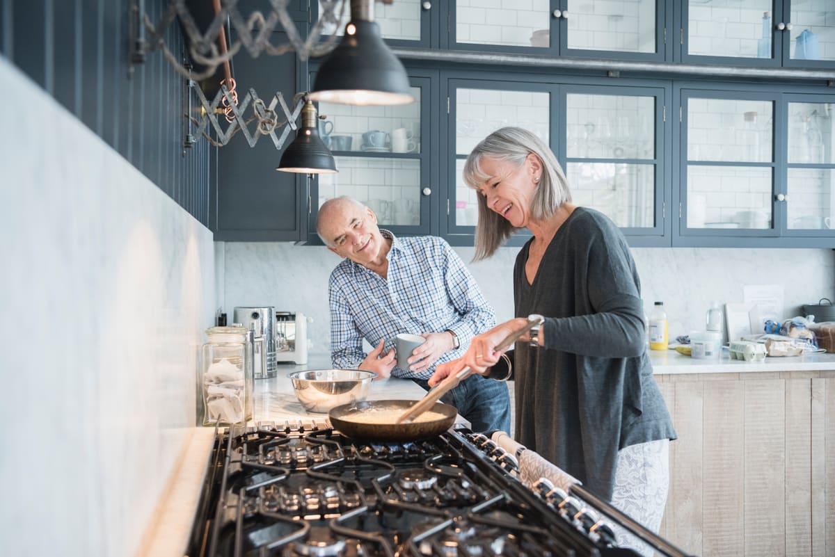 A couple in their sixties cooking together at the stove, laughing