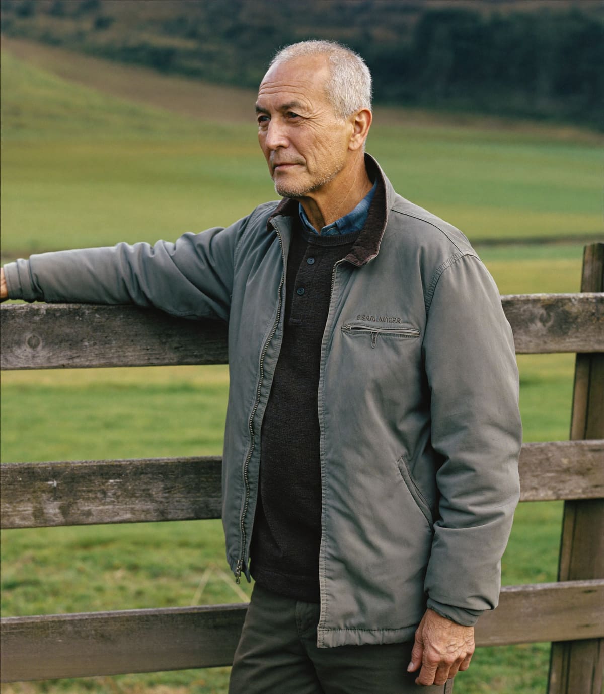A man resting a hand on a farm gate beside a paddock in the Manawatū